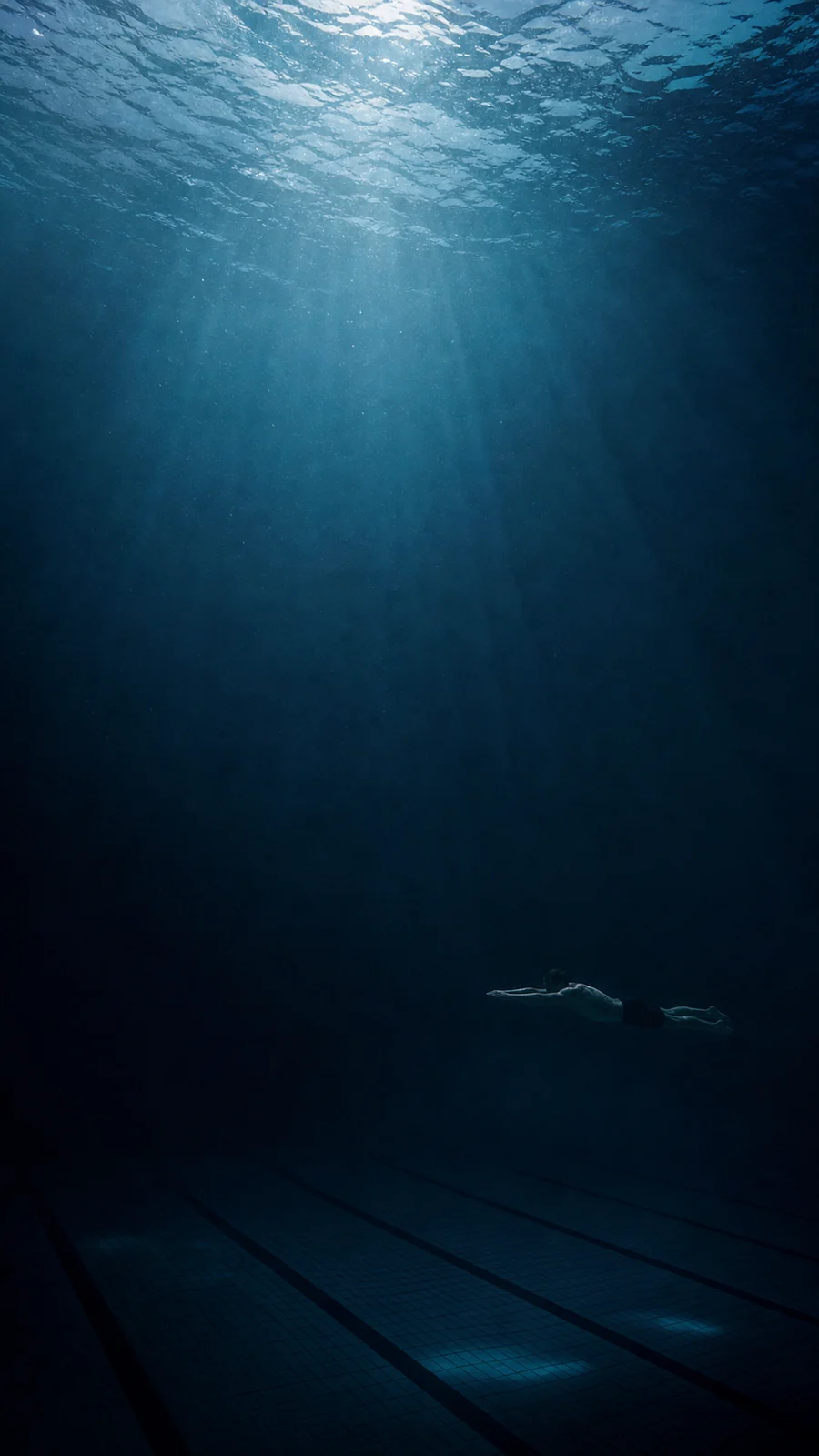 Ein einzelner Schwimmer zieht ruhig durch ein dunkles, stilles Schwimmbecken.