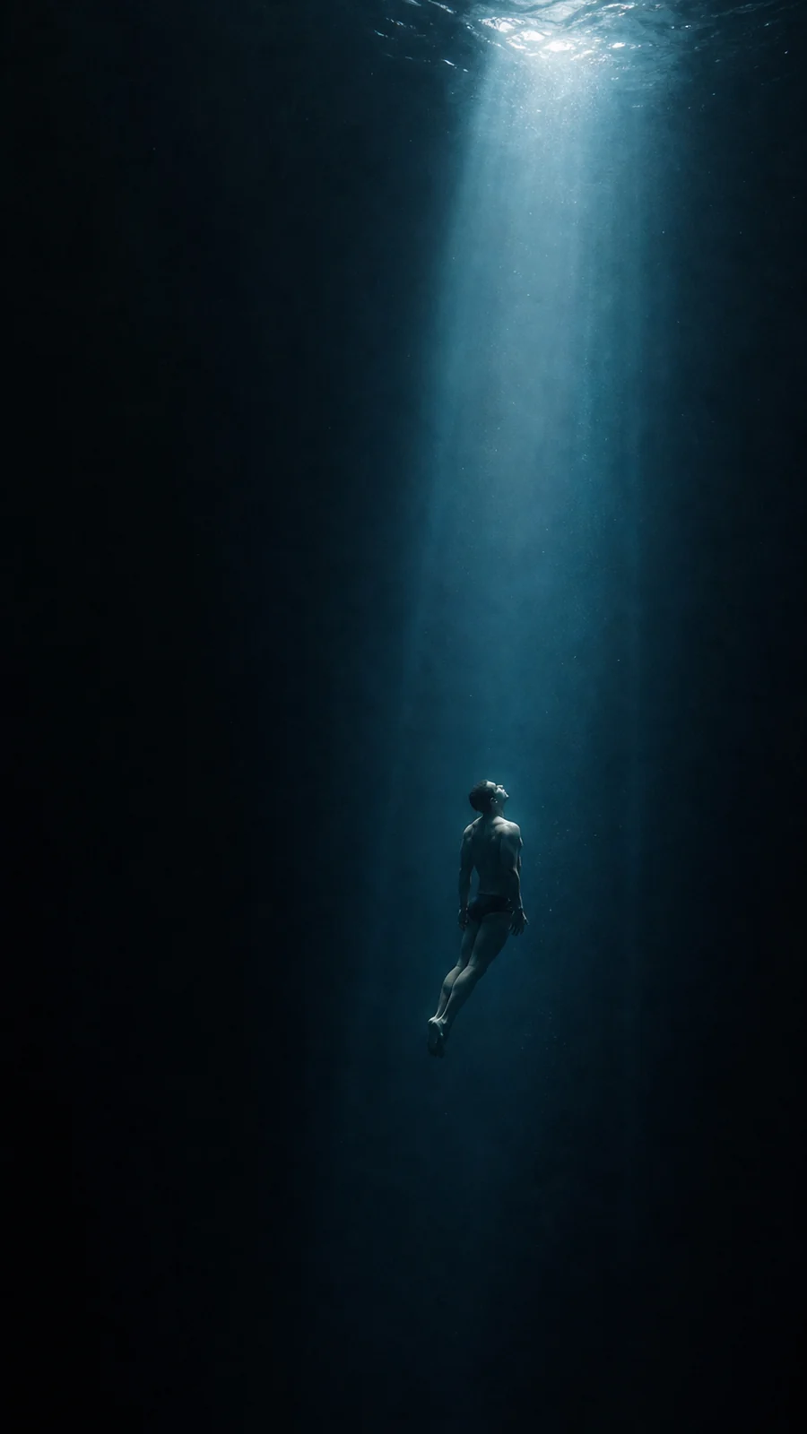 Ein Mensch schwebt ruhig in einem Lichtstrahl in der tiefen Unterwasserwelt.